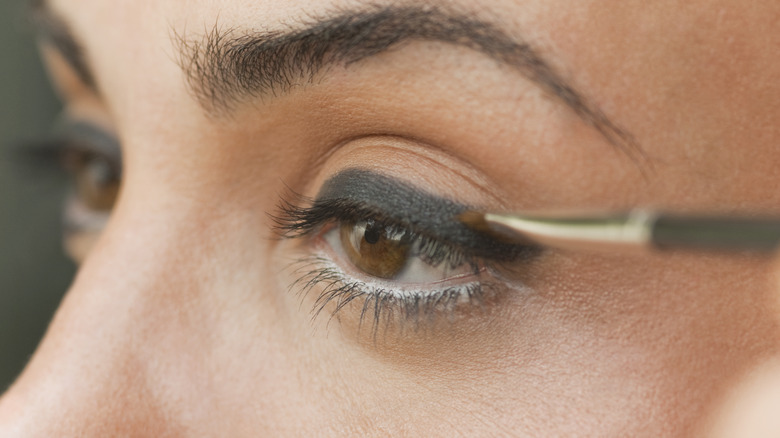 A woman applying thick eyeliner with a brush.