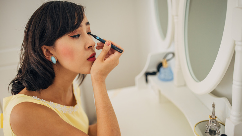 A woman applying liquid eyeliner in the bathroom mirror