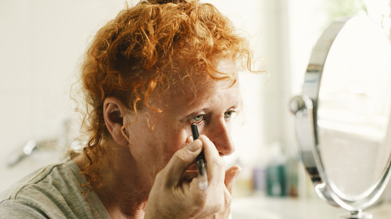 A woman with red hair applying eyeliner to lower lid