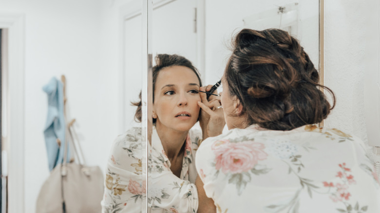 Woman with floral shirt applying eyeliner