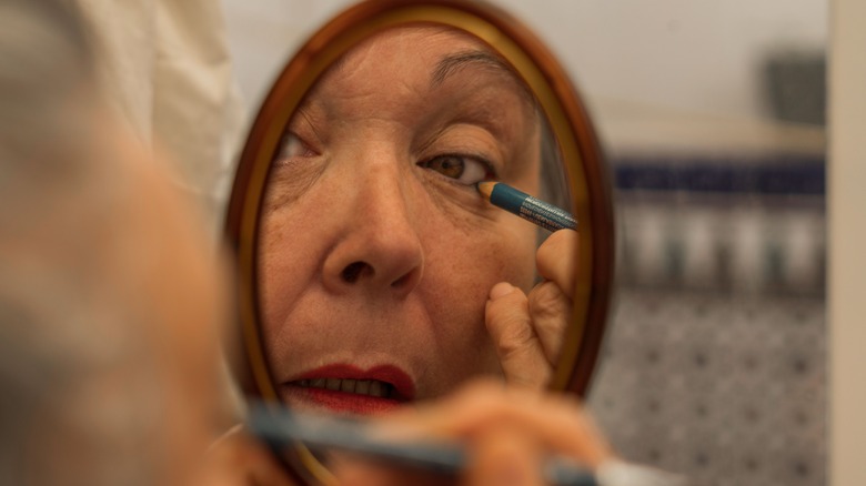 Mature woman applying blue eyeliner