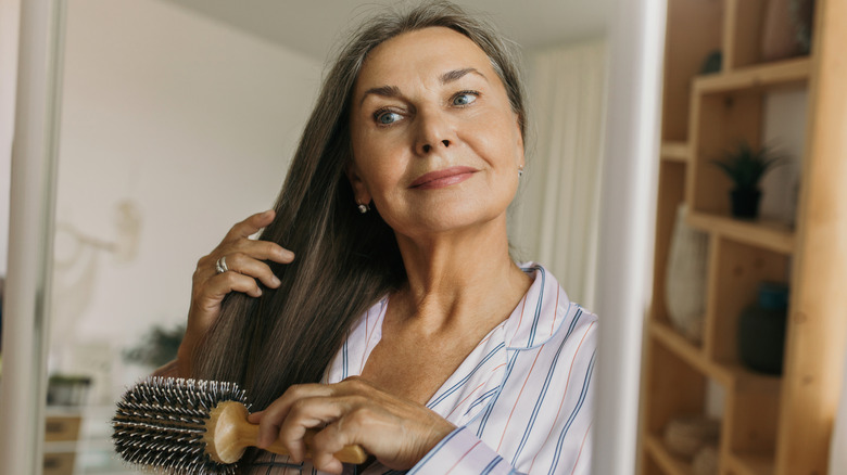 An older woman brushing her hair with a round brush.