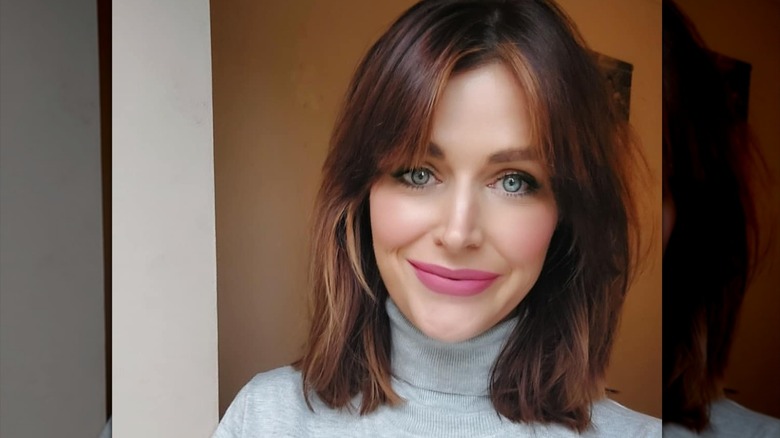 A woman smiling with pink lipstick and a lob haircut