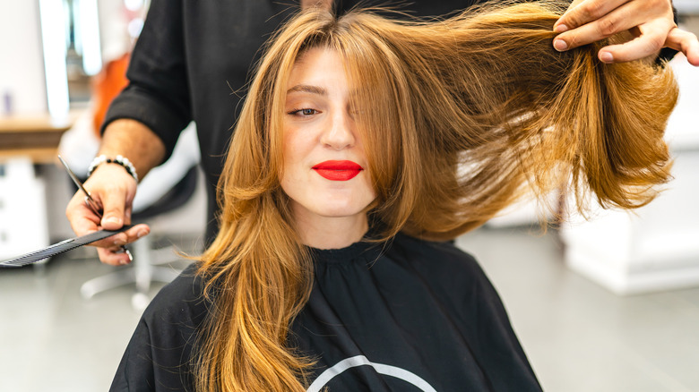 A woman getting her hair cut, with the stylist showing her long, layered locks