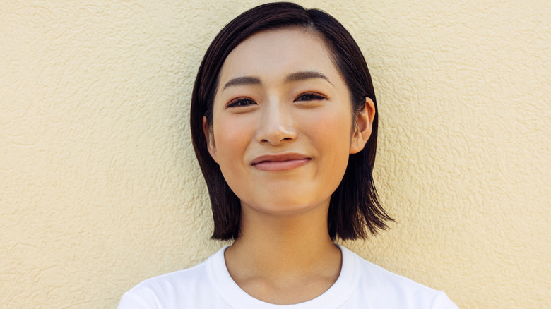 Woman with a sleek side-parted lob standing against a wall