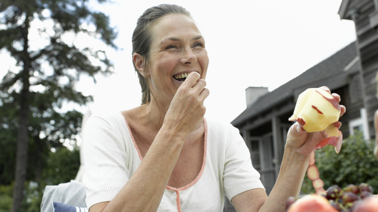 An older woman eating an apple and laughing.