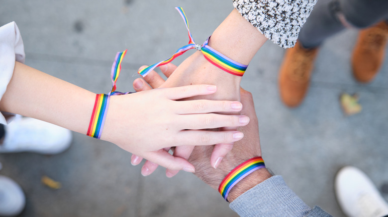 Three hands wearing pride bracelets