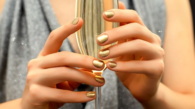 Hands with gold manicure holding champagne