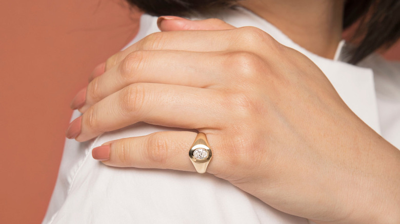 woman wearing a signet diamond engagement ring on hand that's resting on shoulder