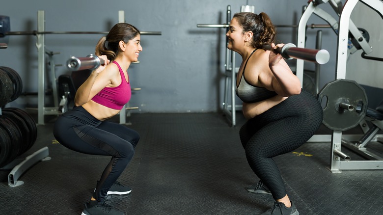 Two women squatting with the bar