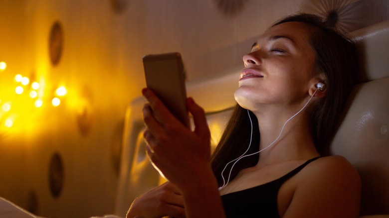 Woman with earbud headphones in bed