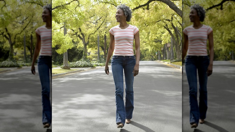 A middle-aged woman walking in straight-leg jeans and a striped top.