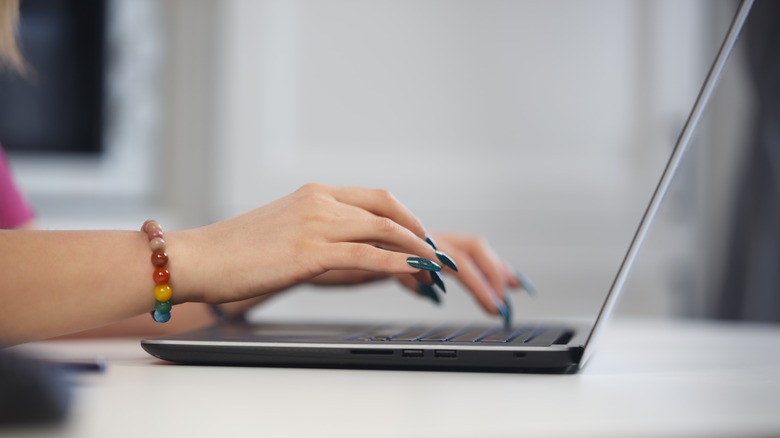 Person with long blue nails typing on a laptop keyboard