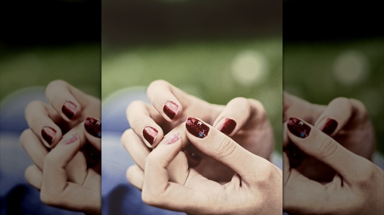 Person picking off burgundy polish from their nails