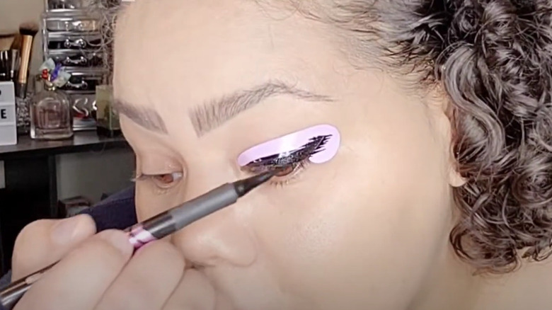 Woman applying liquid eyeliner with a stencil