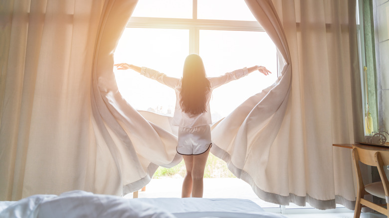 woman opening curtains on sunny day