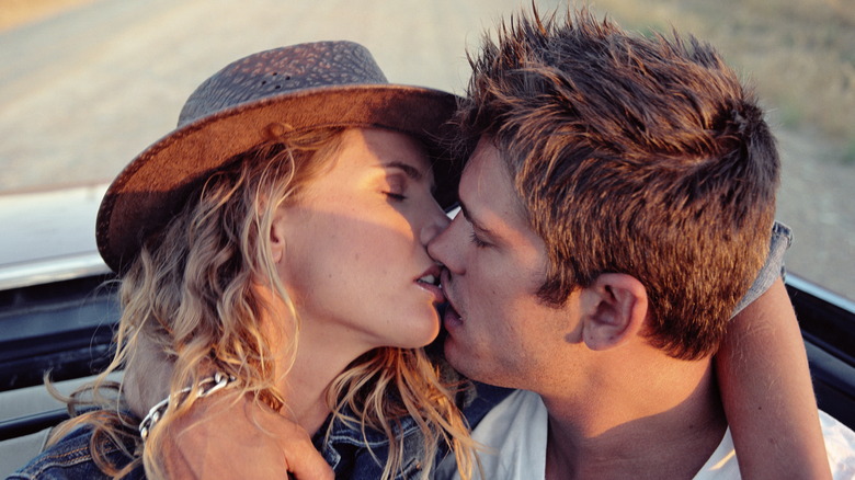 A couple kissing passionately in the back of a car.