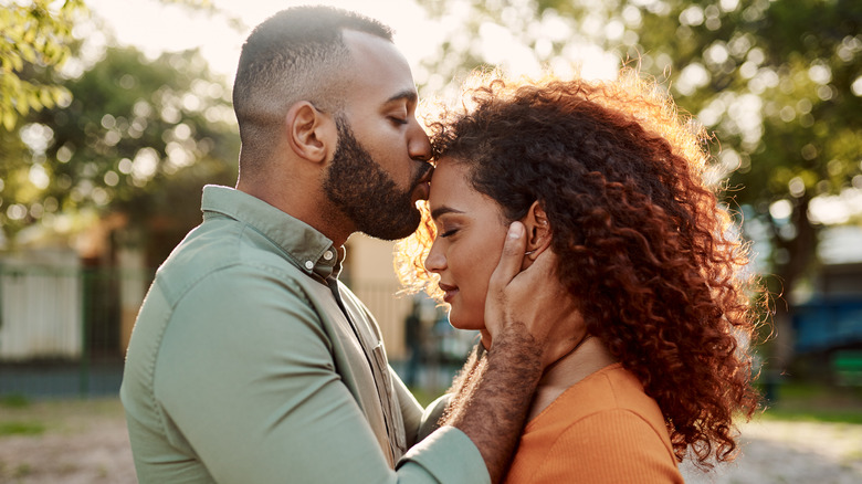 A man kissing a woman's forehead outside.