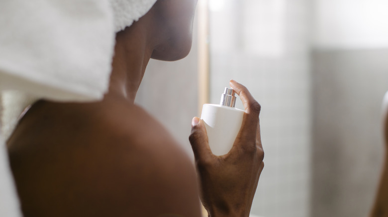 A person in a bath towel spraying perfume