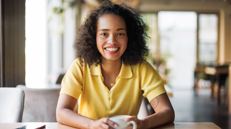 A woman smiling with red lips and holding a teacup