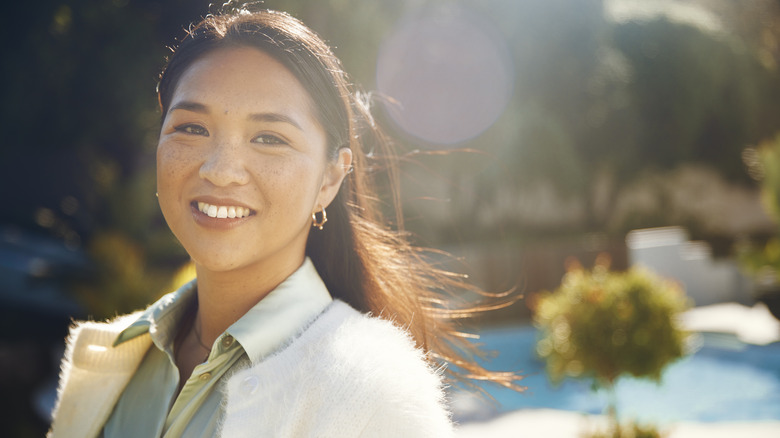 A woman smiling outside with the sun shining on her skin