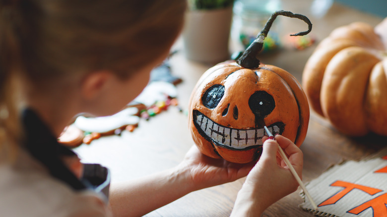 Woman painting detailed face on pumpkin