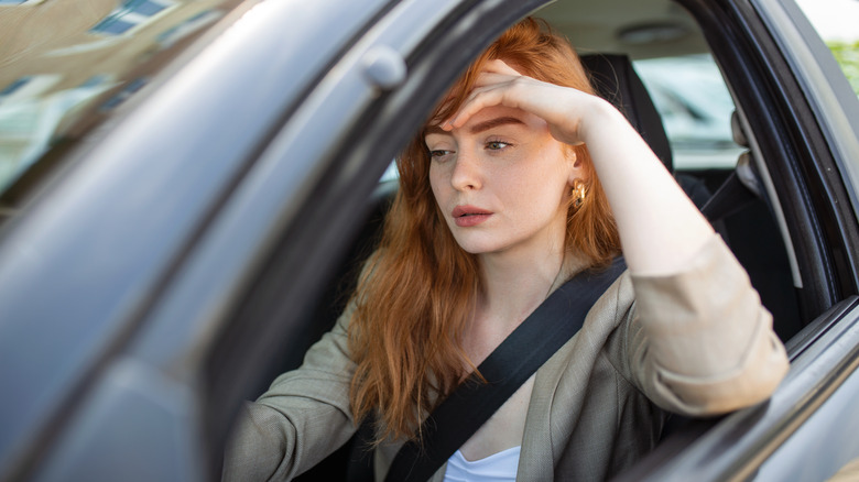 Woman rests forehead on hand car