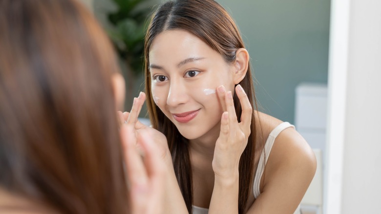 Woman applying sunscreen to cheeks in the mirror