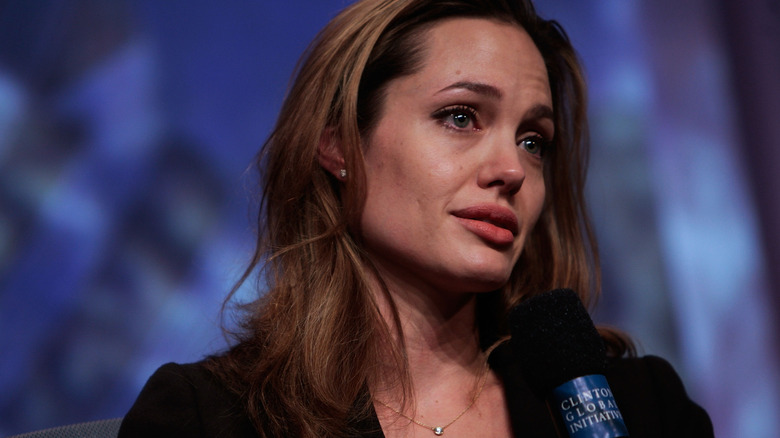 Angelina Jolie wears minimal makeup and a black top while speaking on a panel.