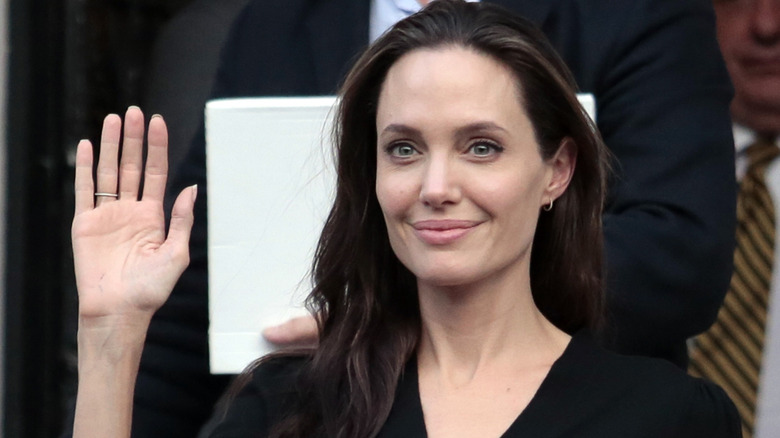 Angelina Jolie wears minimal makeup and loose hair while waving her hand.