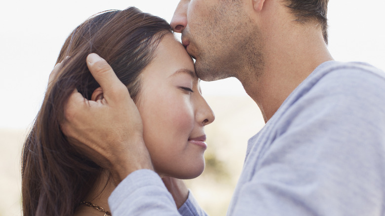 Man kissing Asian woman on forehead