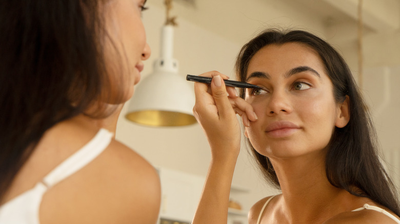 Woman applying eyeliner in mirror 