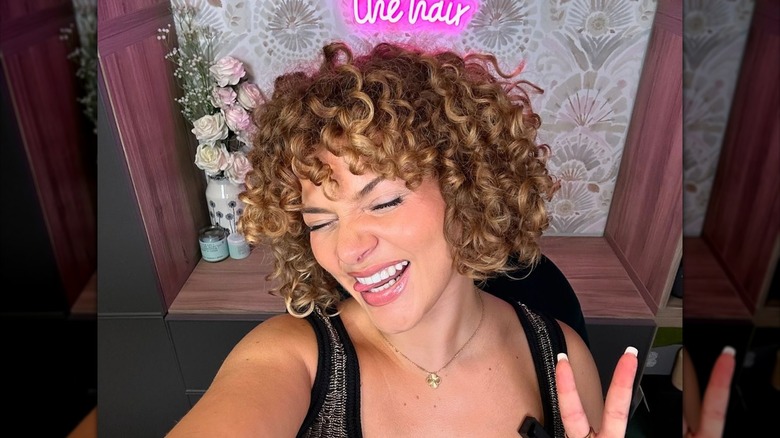 A woman with a curly pageboy cut making a peace sign.