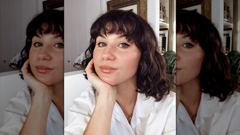 A woman with wavy bangs poses pensively for the camera.