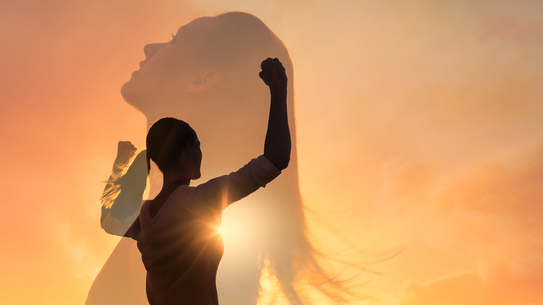 Silhouette images of victorious woman against sunset background