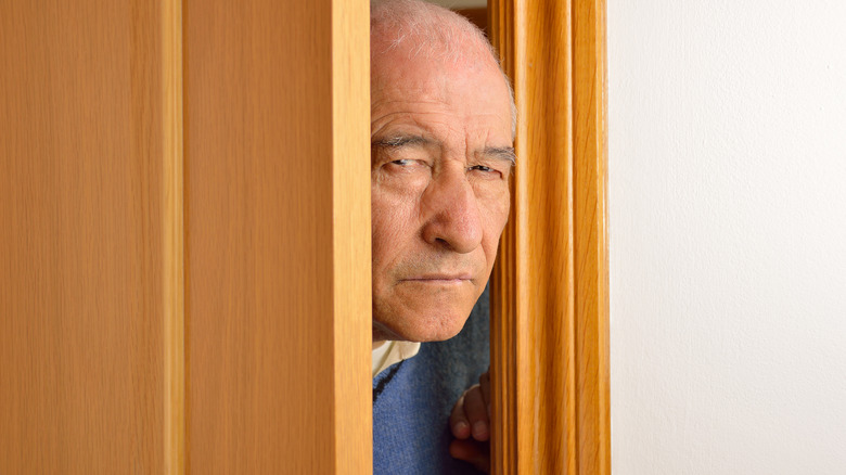 Older man with sinister expression peering in doorway