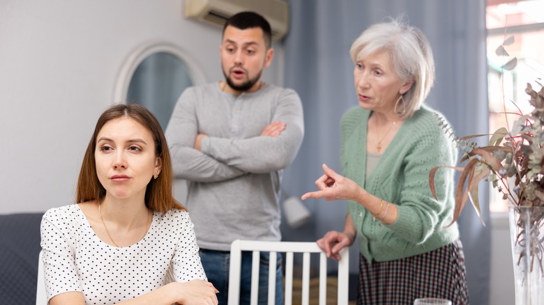 Older woman and younger man arguing with young woman in foreground with her back turned to them