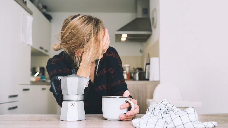 Woman holding head and coffee mug