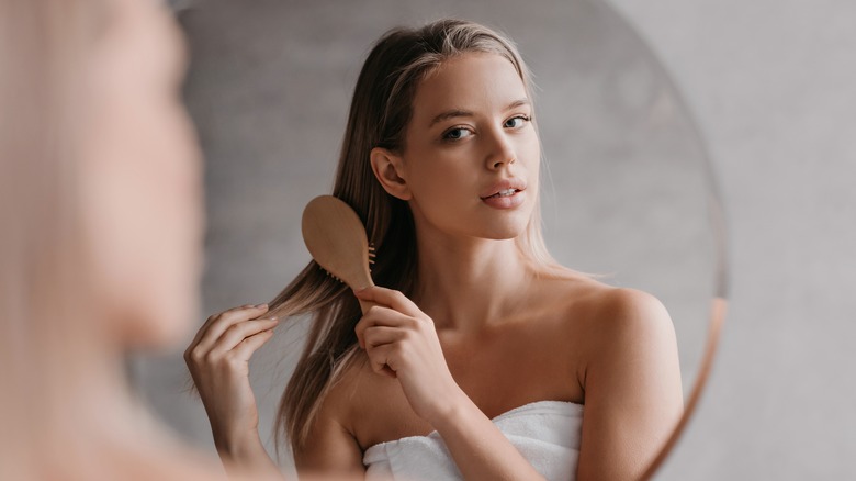 Woman brushing hair in bathroom mirror