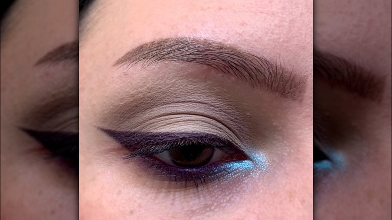 Closeup of eye with purple eyeliner wing and blue inner corner highlight 
