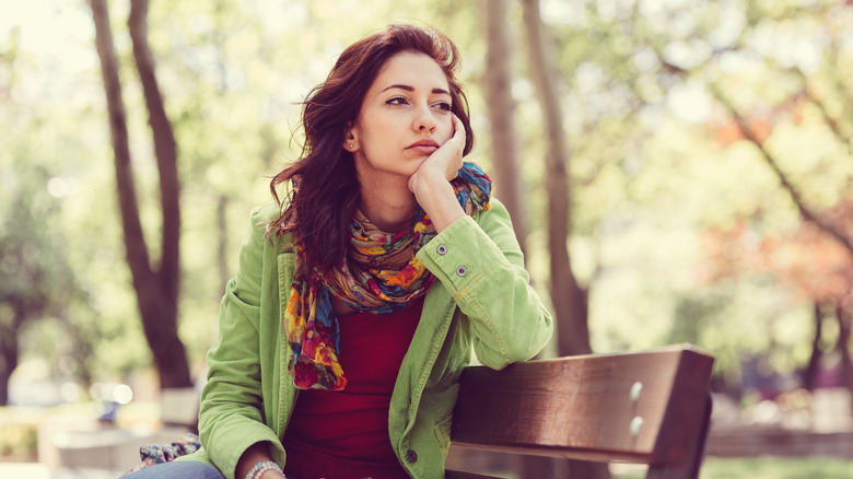 Woman resting head on hand sitting on park bench