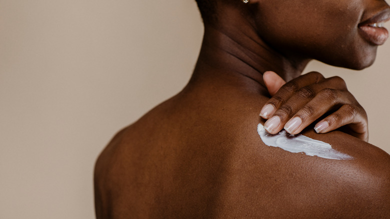 woman applying cream to shoulder 