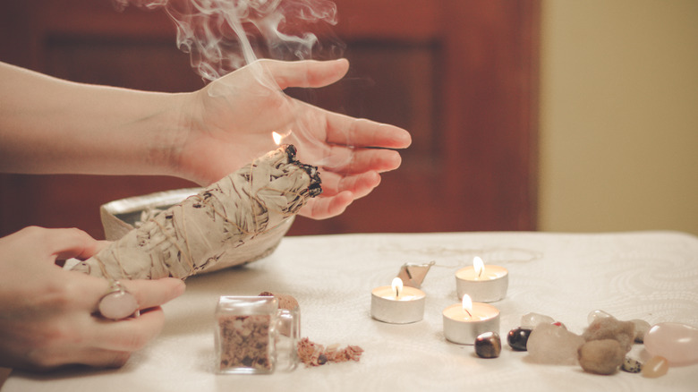 Hand holding a burning sage bundle over a table