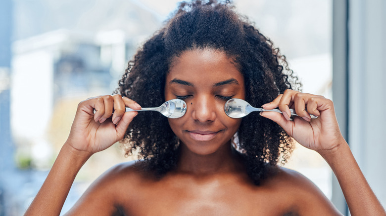 Woman pressing spoons under eyes