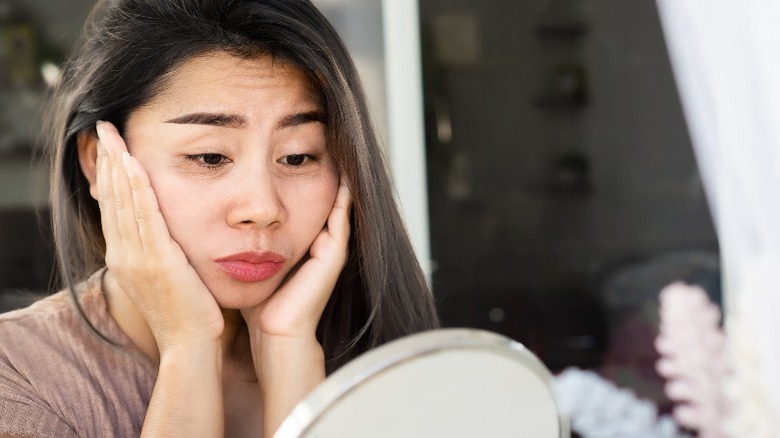 Woman looking in mirror, hands on cheeks