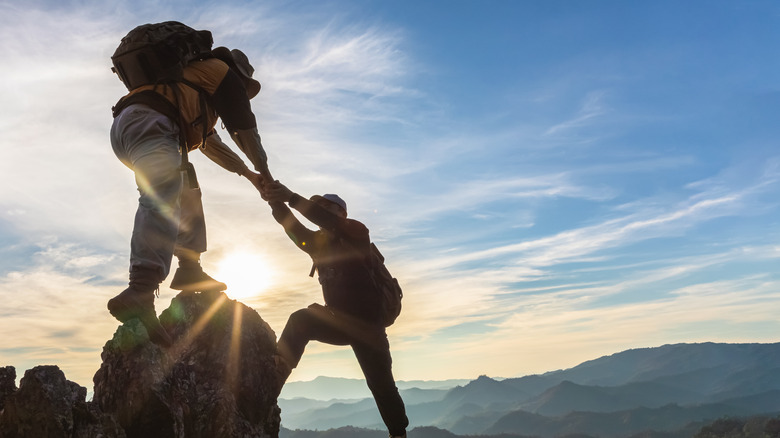 Male hiker helping female hiker ascend a rock