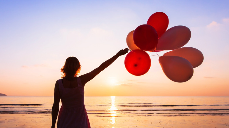 Woman releasing balloons at sunset beach