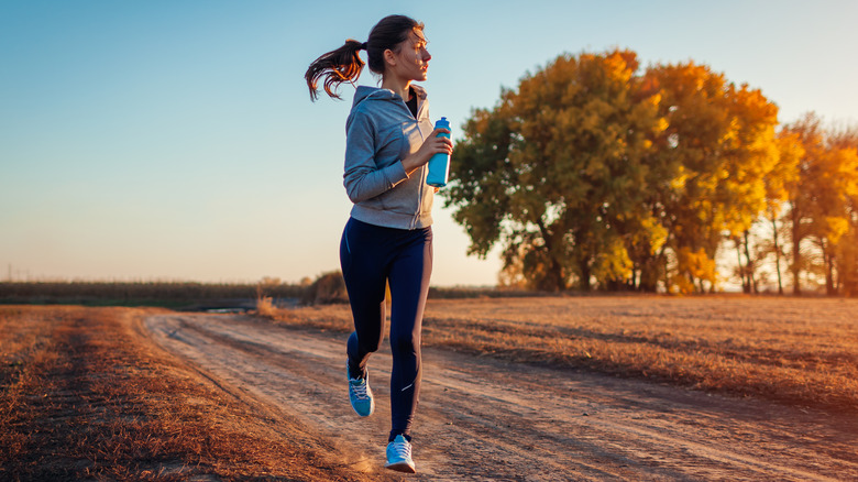 Woman running down empty road overlooking trees