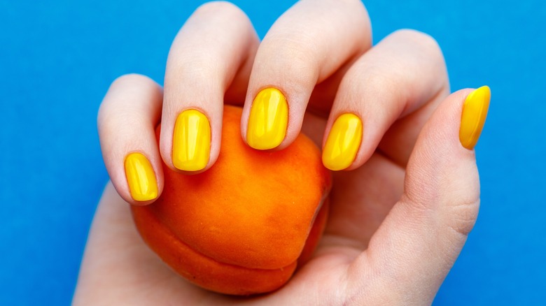 Yellow manicure holding nectarine