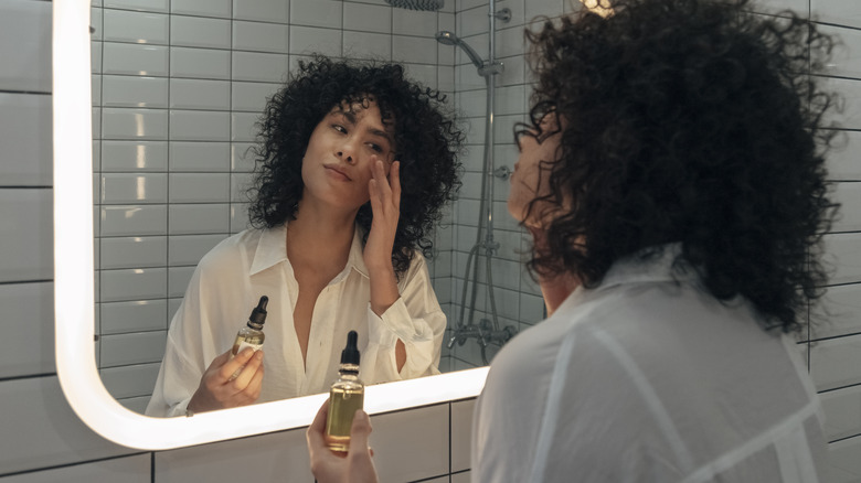 Woman applying face oil in mirror